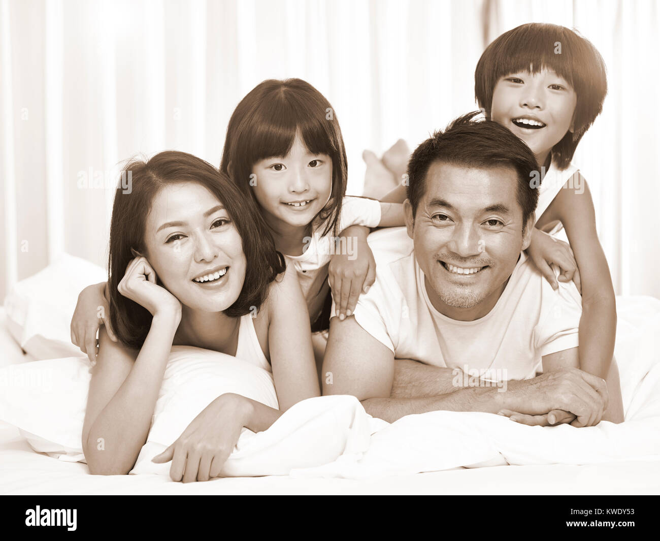 happy asian family with two children having fun in bed at home, black and white sepia toned. Stock Photo