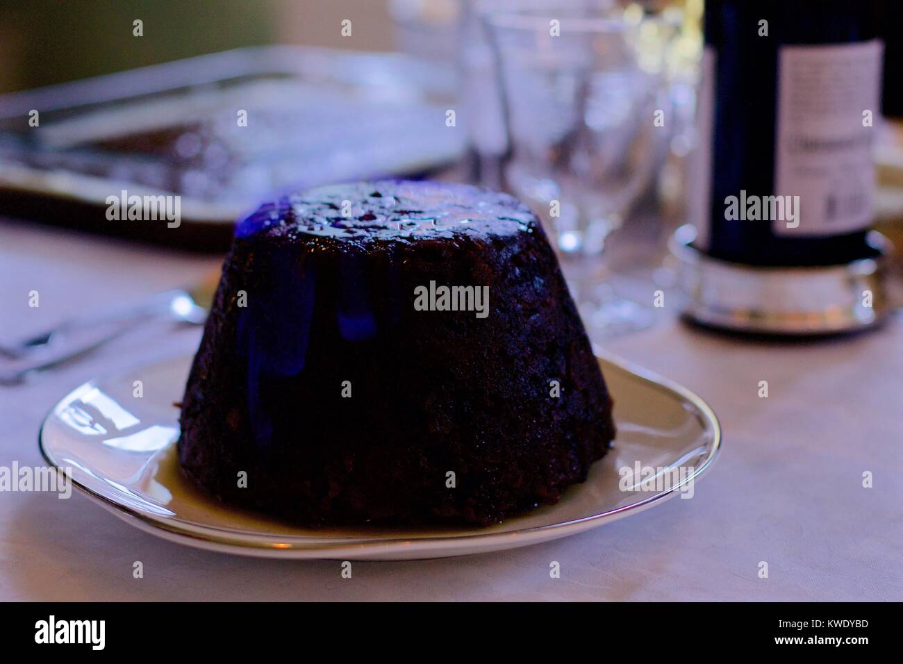 Flaming Christmas pudding on white tablecloth with drinks in the background, UK Stock Photo