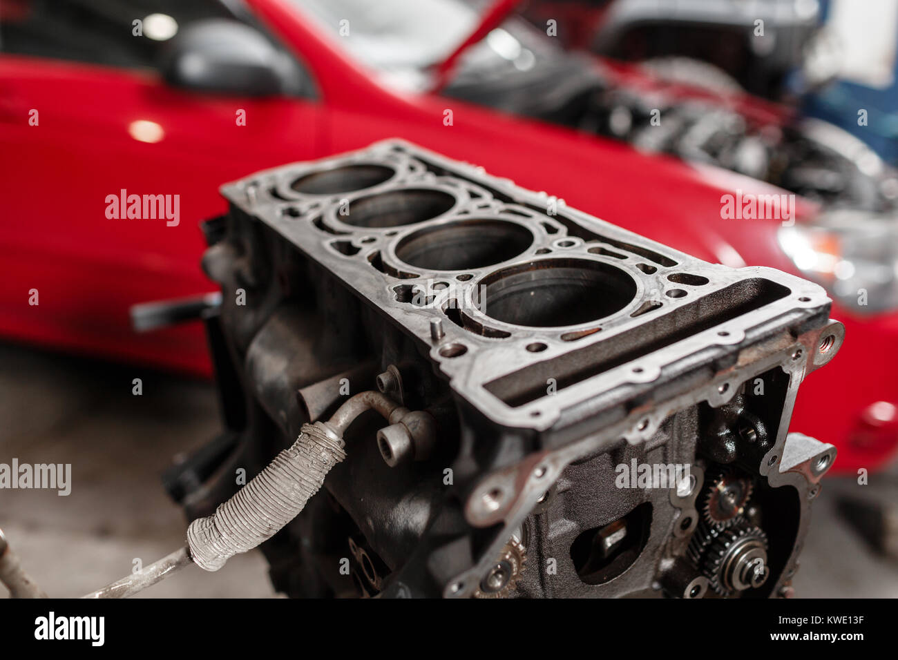 Selective focus. Engine Block on a repair stand with Piston and Connecting Rod of Automotive technology. Blurred red car on background. Interior of a car repair shop. Stock Photo