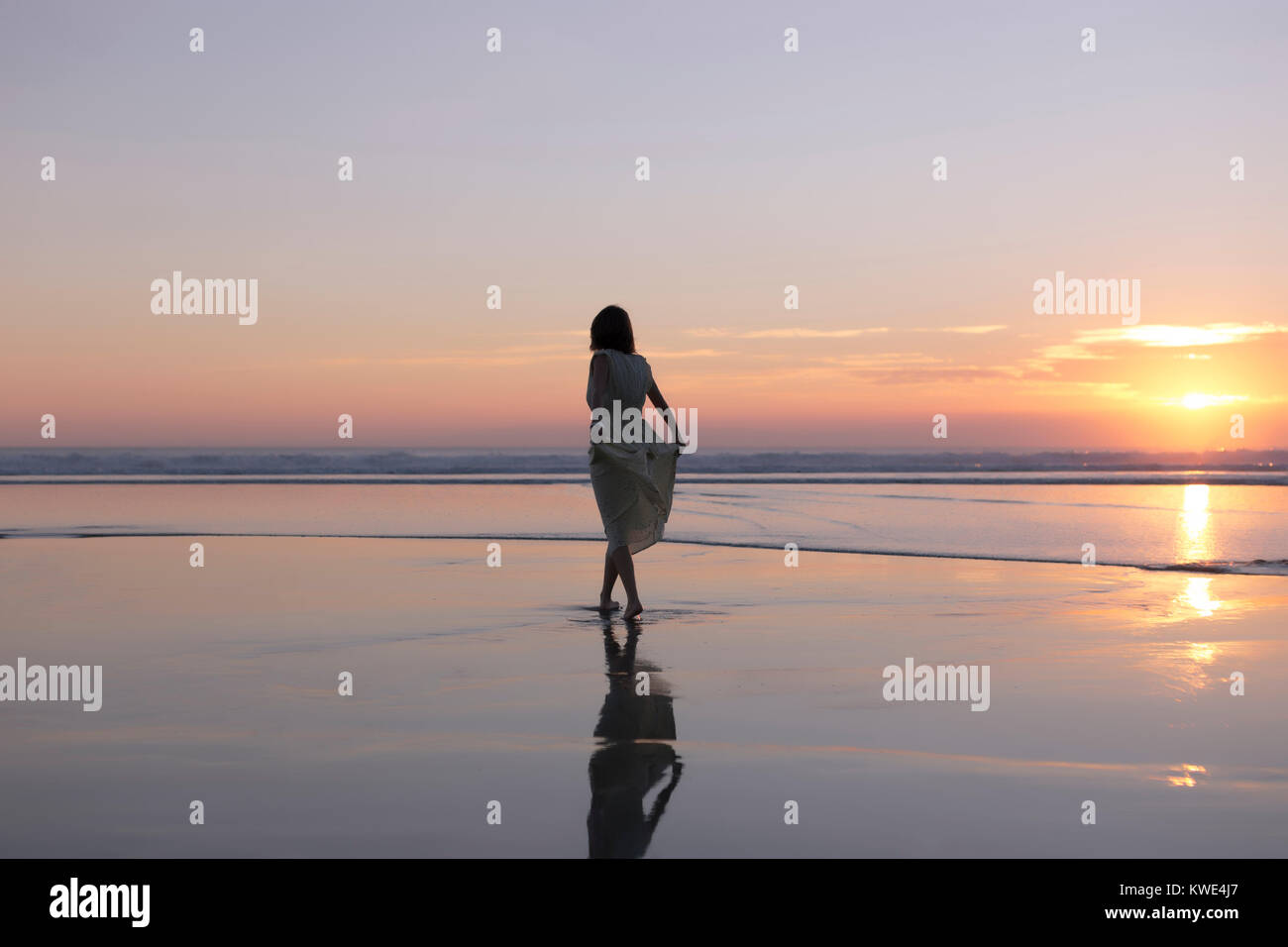 Carefree woman holding dress while walking at beach against sky during sunset Stock Photo