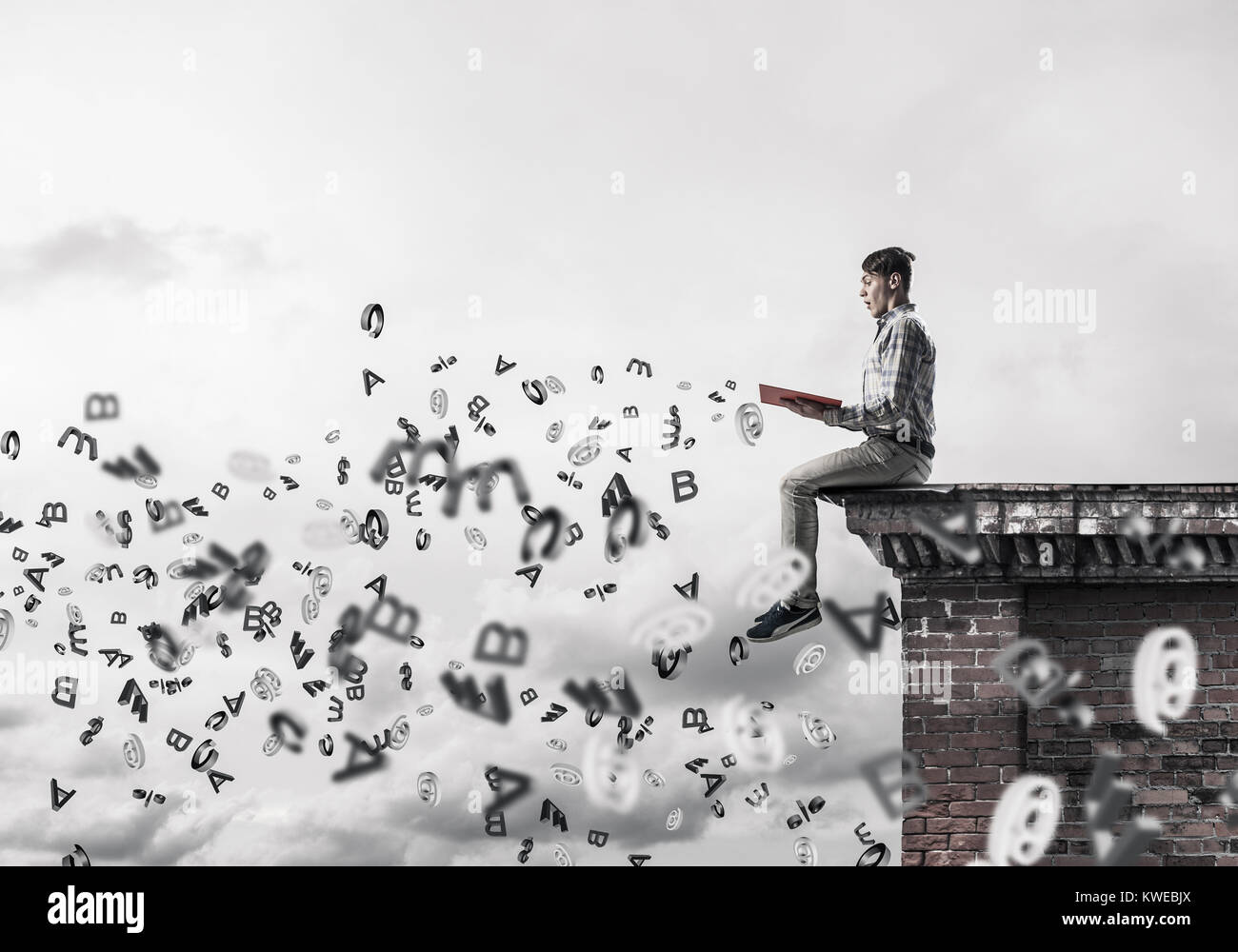 Man on roof edge reading book and symbols flying around Stock Photo