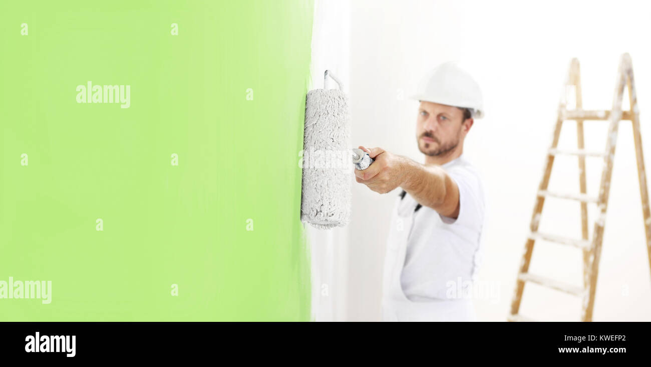 painter man at work with a paint roller, wall painting green color ecological concept, web banner template Stock Photo