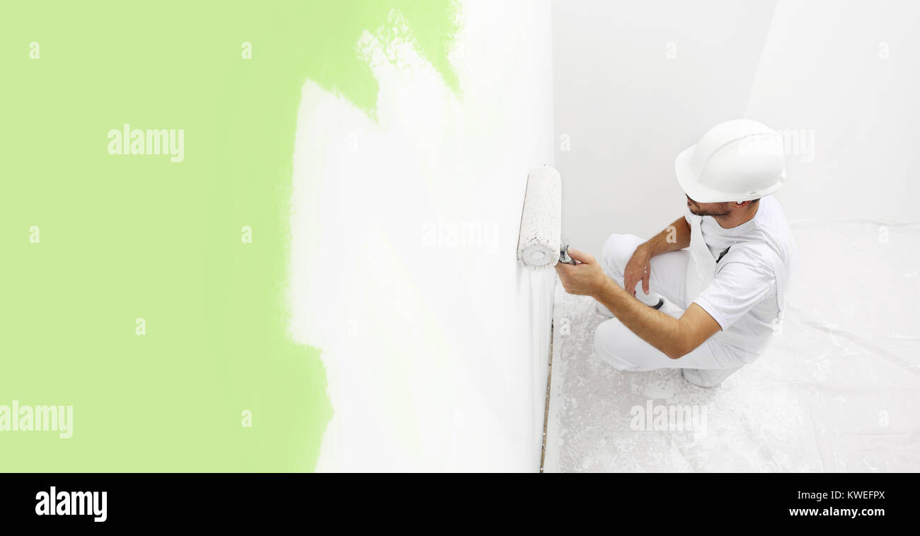 painter man at work with a paint roller, wall painting green color ecological concept, web banner template Stock Photo