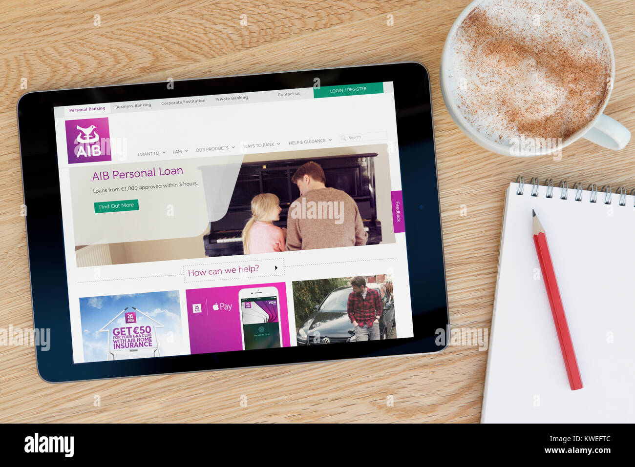 The AIB (Allied Irish Bank) website on an iPad tablet device, resting on a wooden table beside a notepad, pencil and cup of coffee (Editorial only) Stock Photo