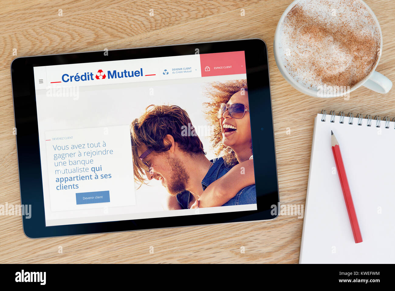 The Credit Mutuel website on an iPad tablet device, resting on a wooden table beside a notepad, pencil and cup of coffee (Editorial only) Stock Photo