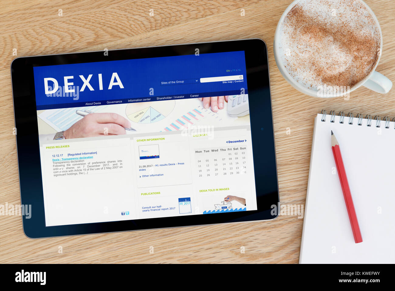 The Dexia Bank website on an iPad tablet device, resting on a wooden table beside a notepad, pencil and cup of coffee (Editorial only) Stock Photo