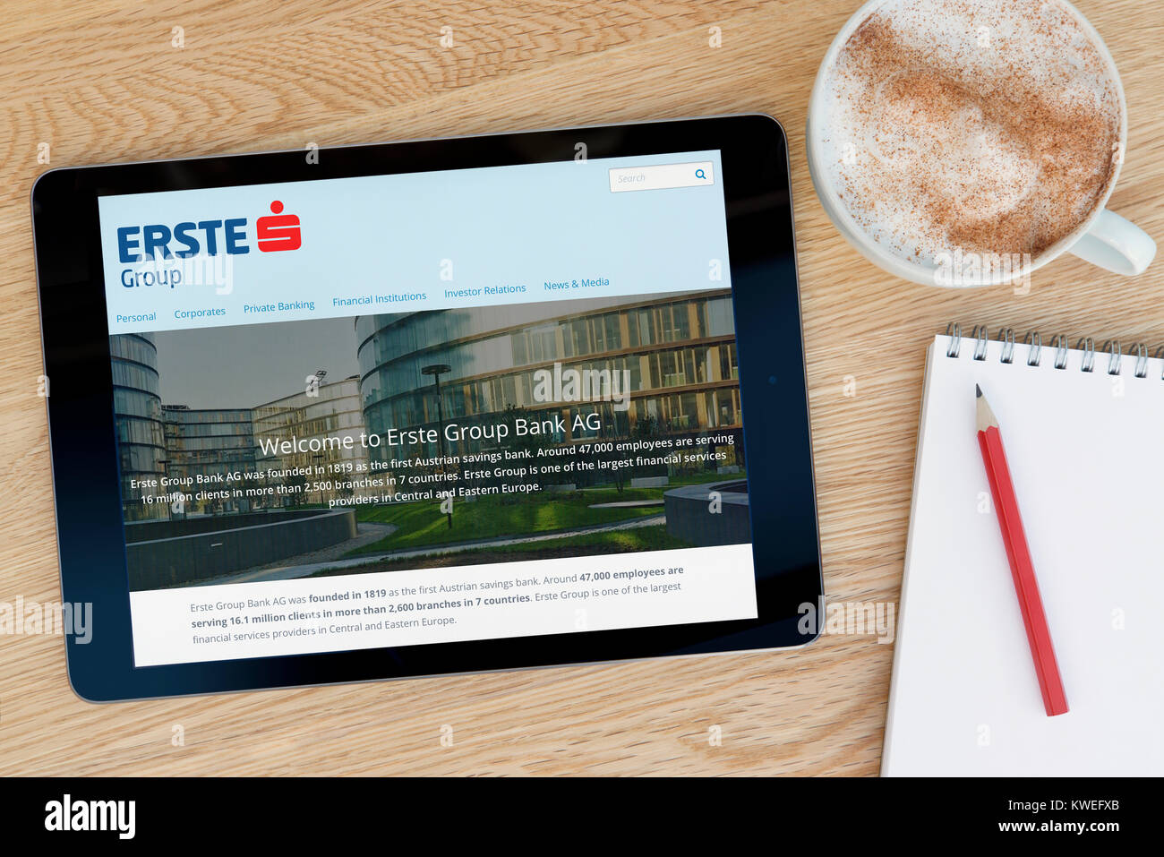 The Erste Group website on an iPad tablet device, resting on a wooden table beside a notepad, pencil and cup of coffee (Editorial only) Stock Photo