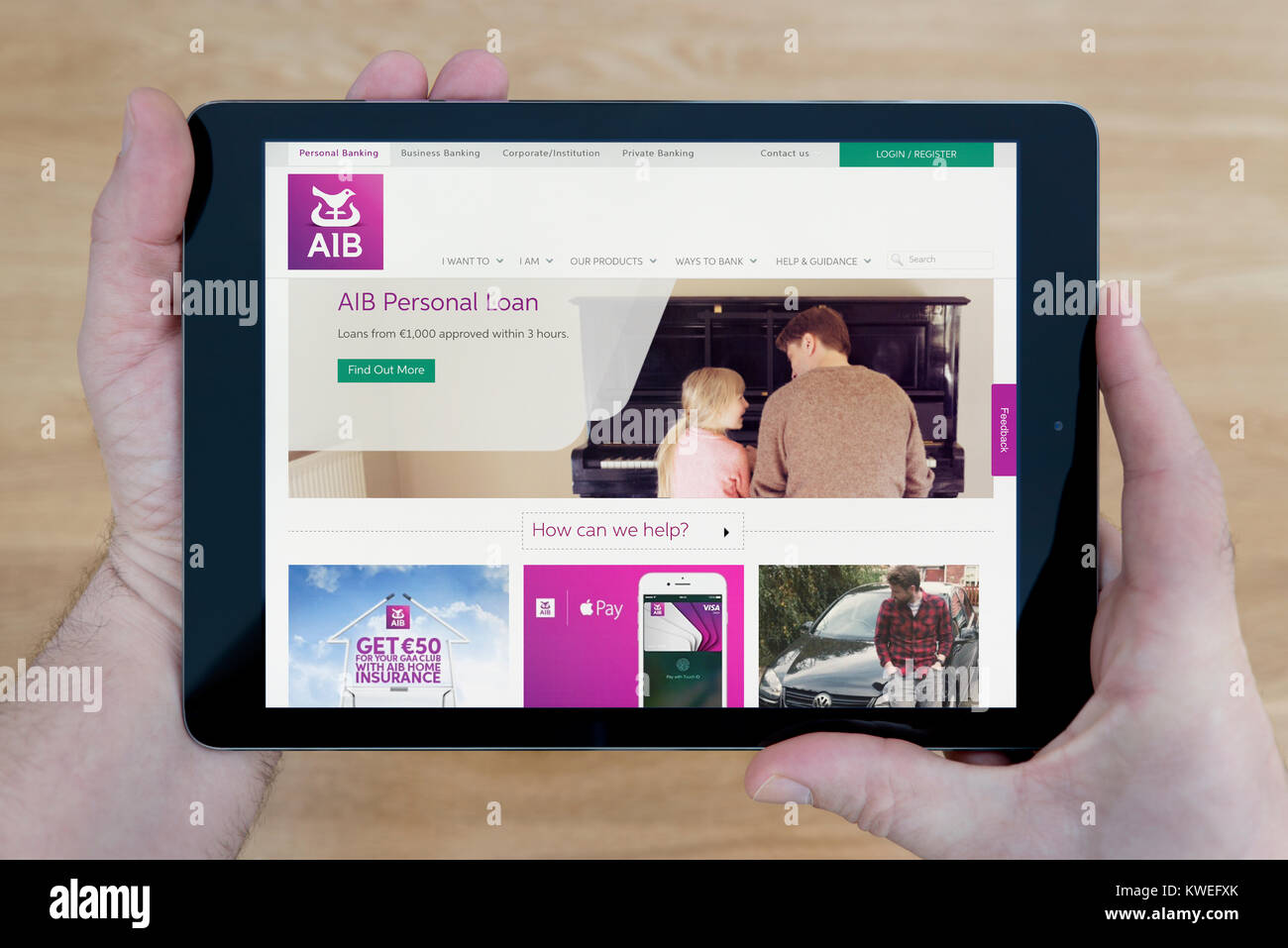 A man looks at the Allied Irish Bank (AIB) website on his iPad tablet device, shot against a wooden table top background (Editorial use only) Stock Photo