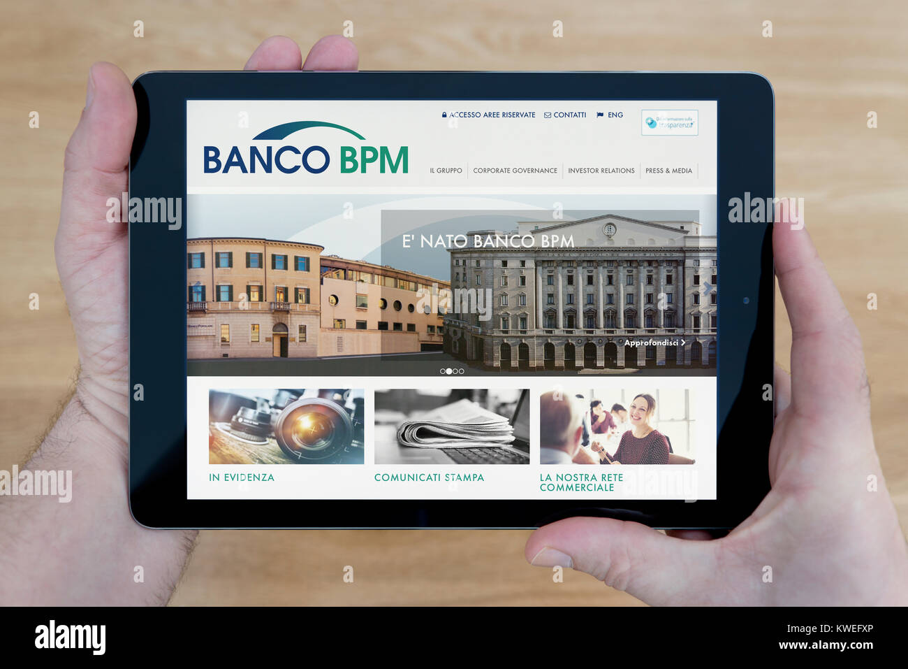 A man looks at the Banco BPM website on his iPad tablet device, shot against a wooden table top background (Editorial use only) Stock Photo