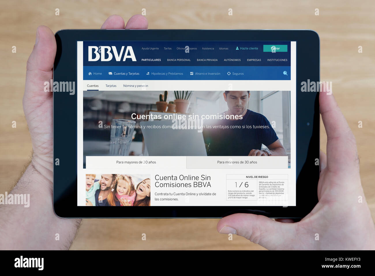 A man looks at the Banco Bilbao Vizcaya Argentaria (BBVA) website on his iPad tablet device, over a wooden table top background (Editorial use only) Stock Photo