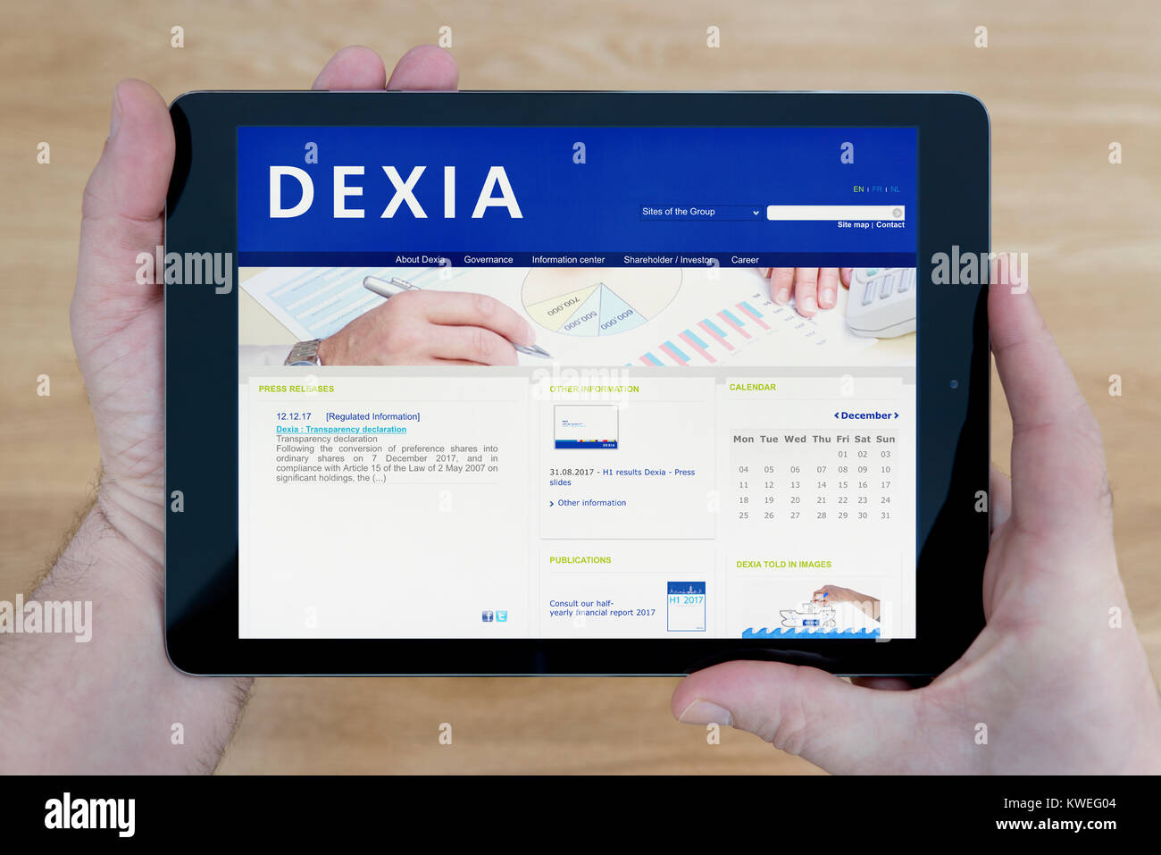 A man looks at the Dexia Bank website on his iPad tablet device, shot against a wooden table top background (Editorial use only) Stock Photo