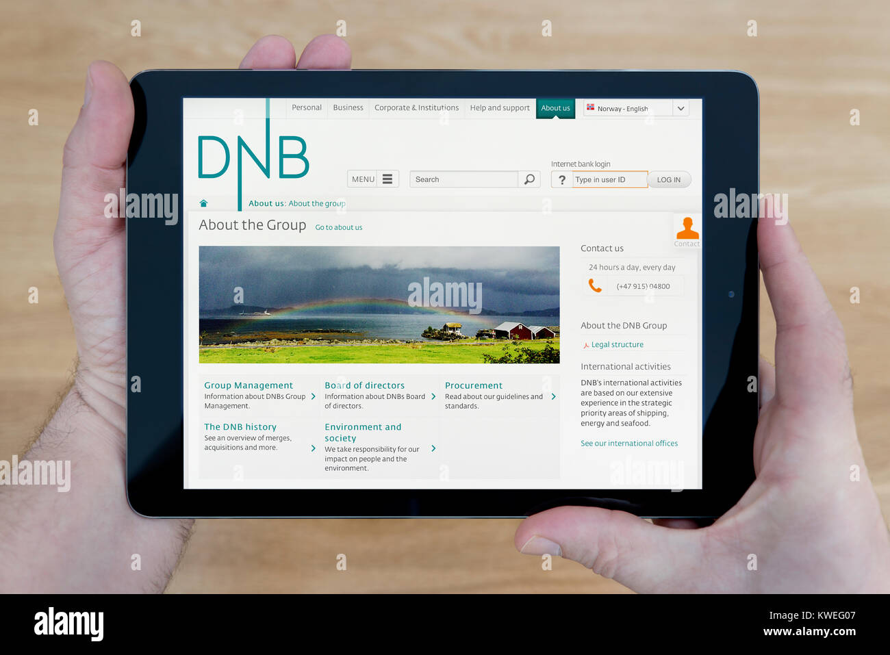 A man looks at the DNB ASA website on his iPad tablet device, shot against a wooden table top background (Editorial use only) Stock Photo