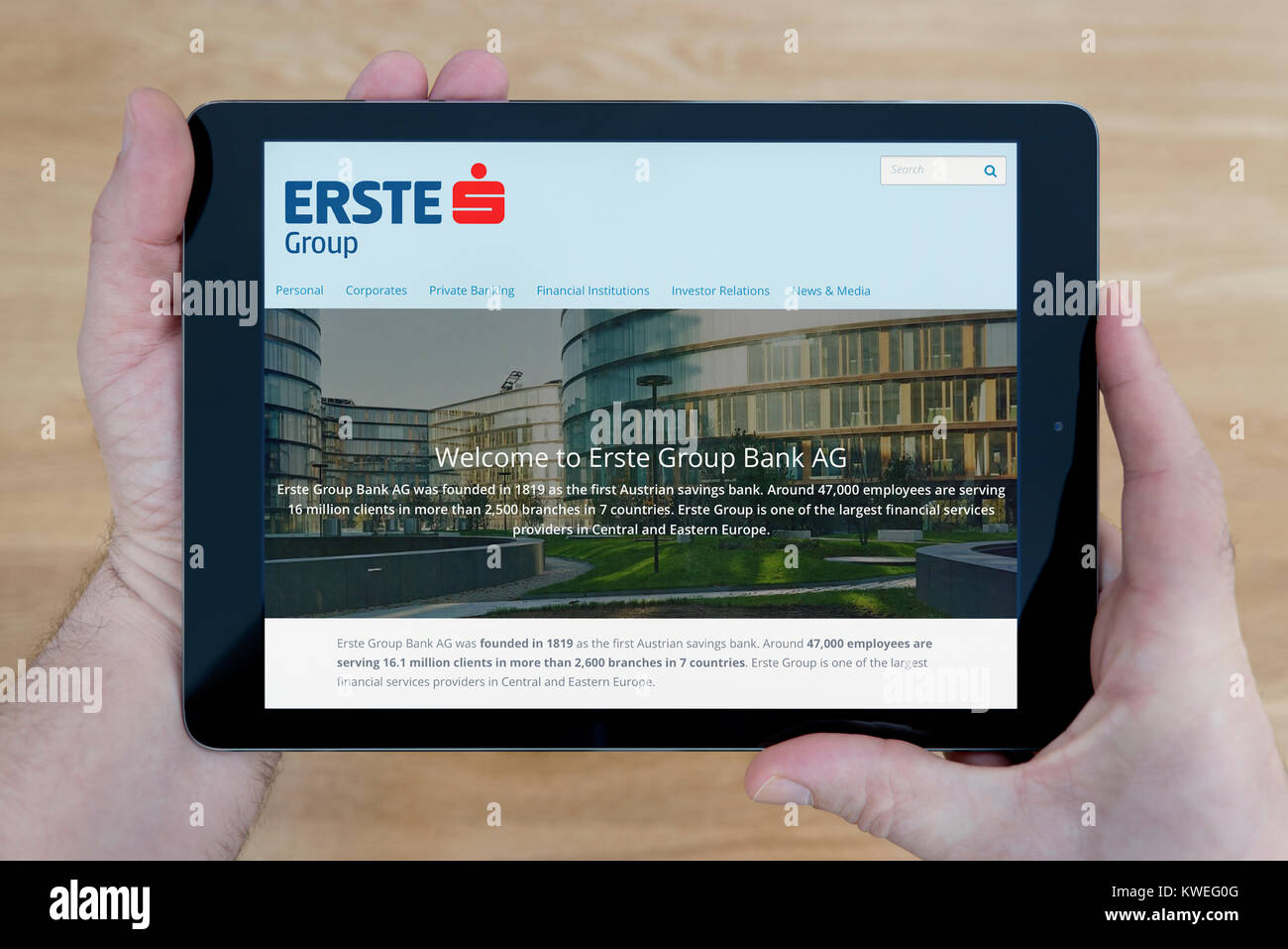 A man looks at the Erste Group Bank website on his iPad tablet device, shot against a wooden table top background (Editorial use only) Stock Photo