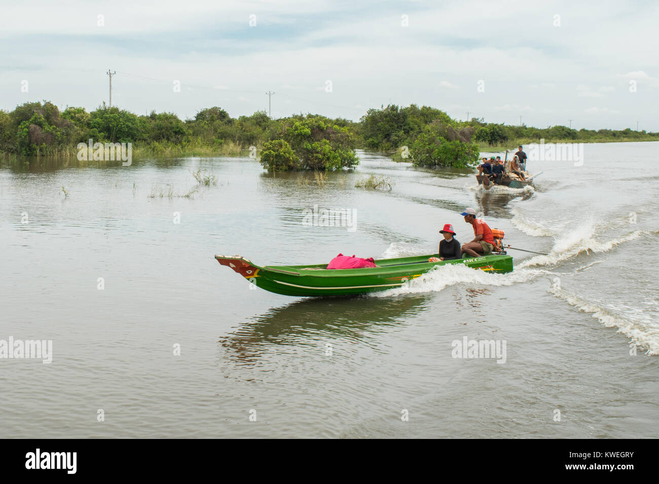 A Cambodian Asian couple sitting on a boat, the man driving the motor powered thin long boat over Tonle Sap Great Lake floodplain Kampong Phluk, Asia Stock Photo