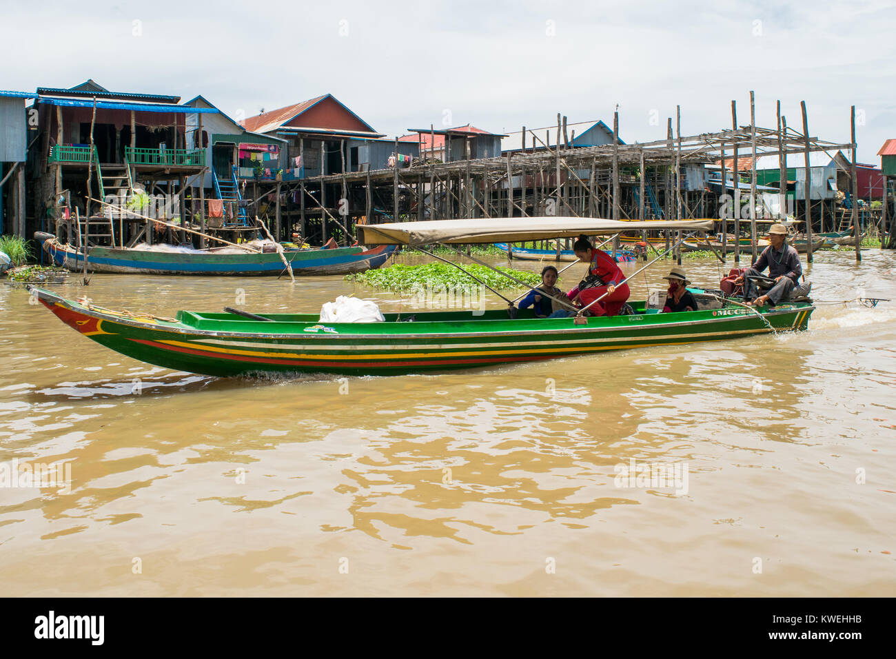Three Cambodia Asian people on a small green long motor powered boat going through the floodplain of Tonle Sap Great Lake. Boat with tent for shade Stock Photo