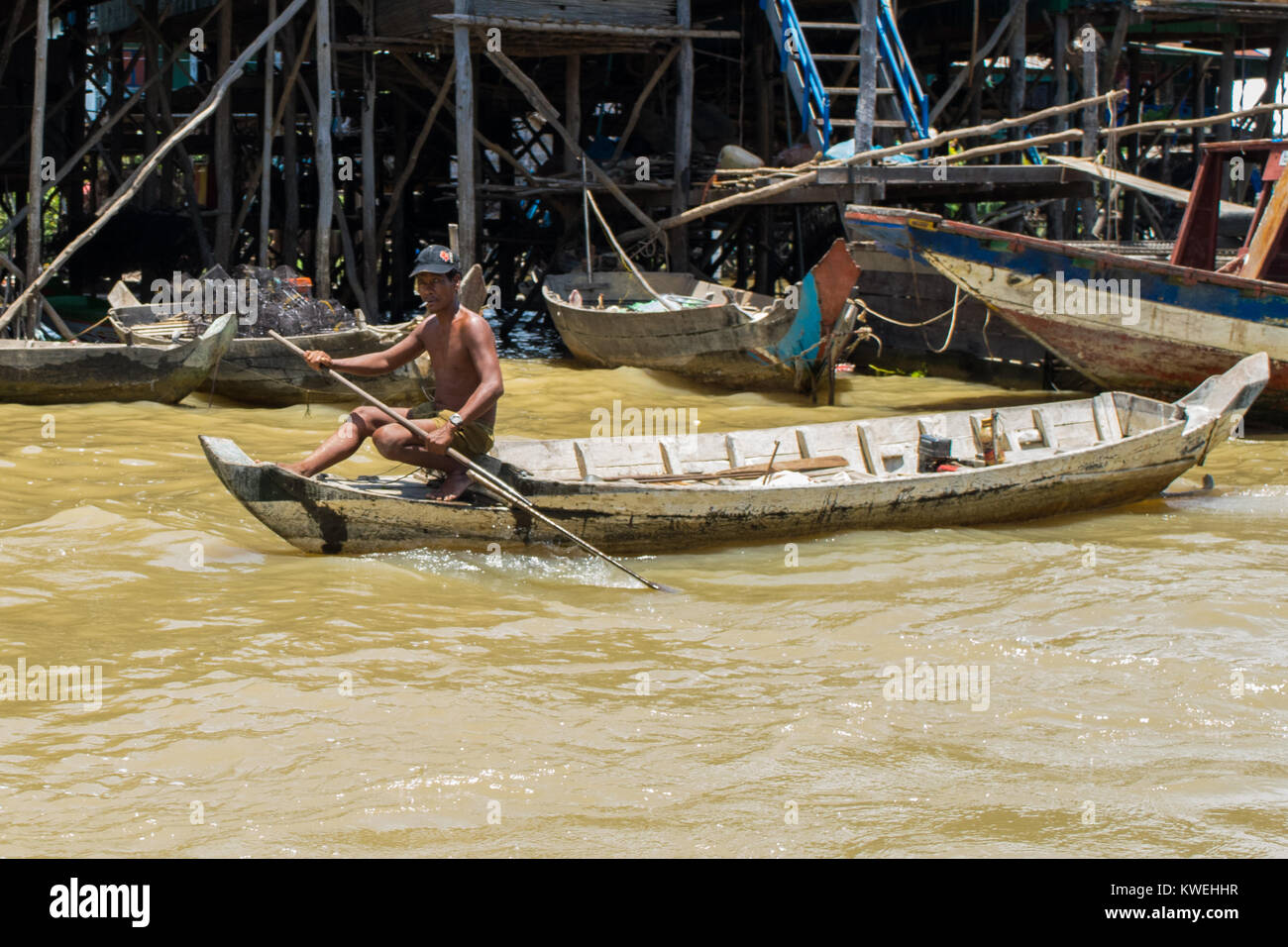 A Cambodian Asian brown skinned man rowing a wooden boat in Kampong Phluk Tone Sap Great Lake floodplain village on stilts, near Siem Reap, Cambodia Stock Photo