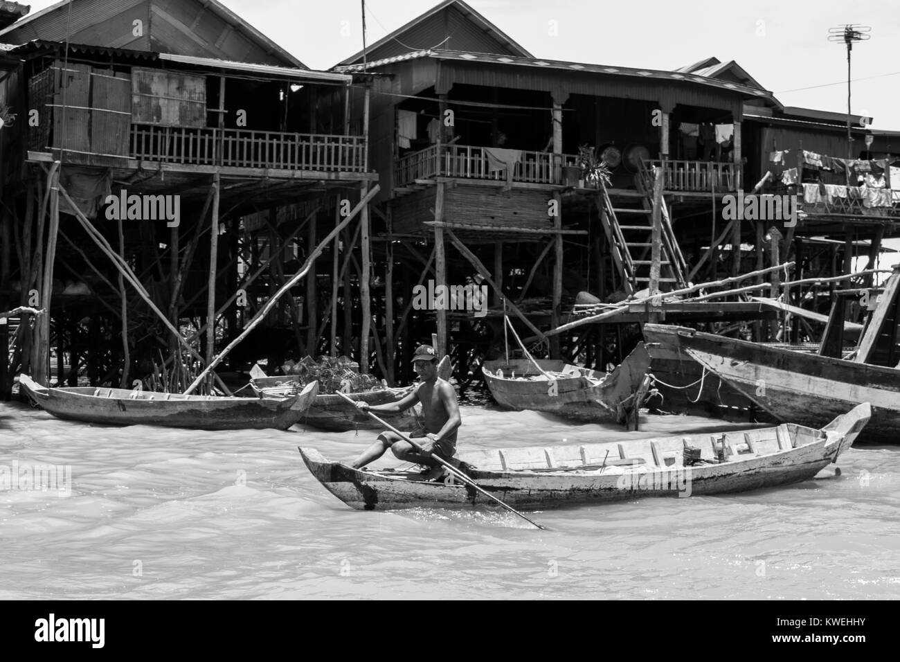 A Cambodian Asian brown skinned man rowing a wooden boat in Kampong Phluk Tone Sap Great Lake floodplain village on stilts, near Siem Reap, Cambodia Stock Photo