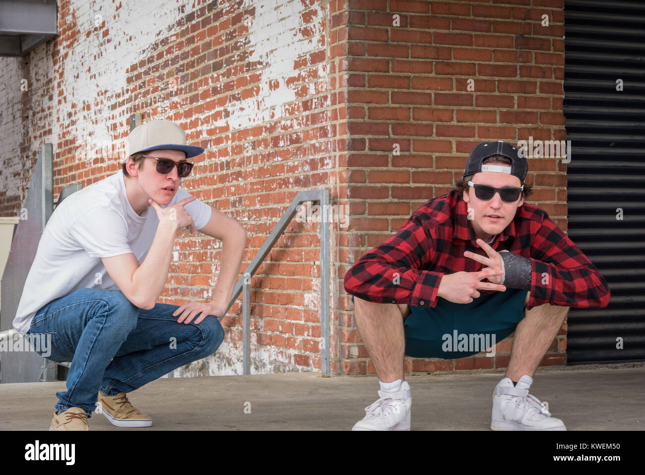 young men in sunglasses and snap back caps posing on loading dock with brick wall Stock Photo