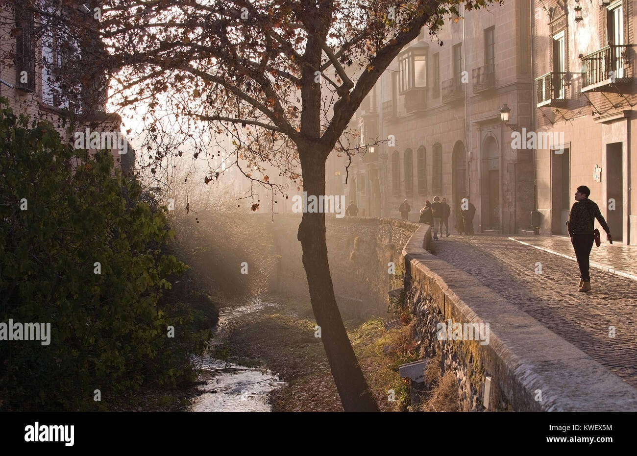 GRANADA, ANDALUCIA, SPAIN - DECEMBER 20, 2017: Woman walks by Carrera del Darro river in afternoon sunhaze on December 20, 2017 in Granada, Andalucia, Stock Photo