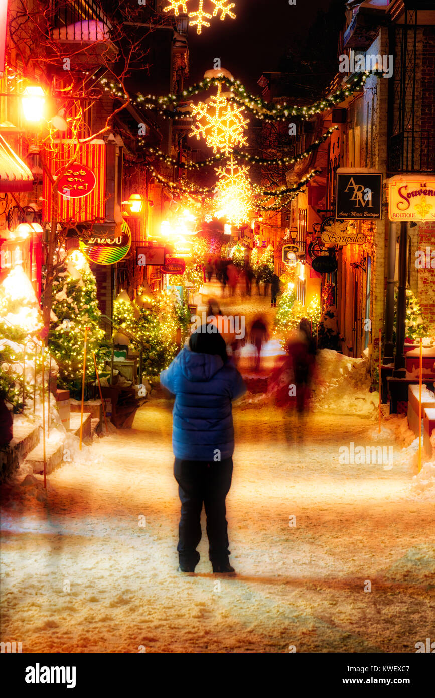 A woman taking pictures of the Christmas decorations and fresh snow in Quebec City's Petit Champlain area at night in Rue Petit Champlain Stock Photo