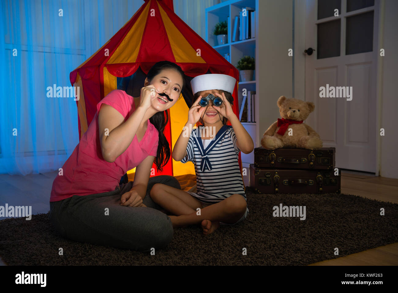 happy beauty girl children as sailor using telescope looking for treasure when she playing game with mother in bedroom at evening. Stock Photo