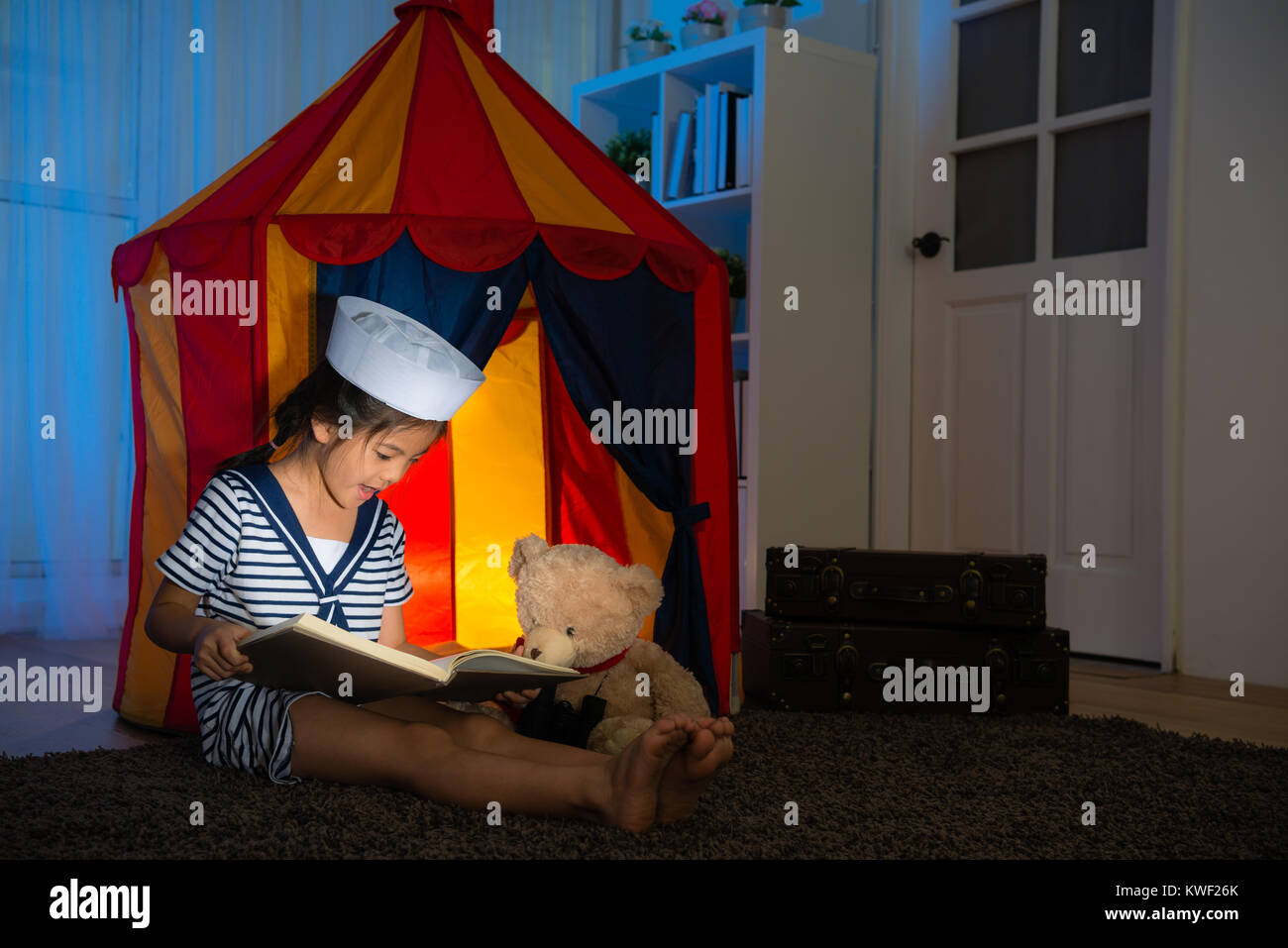 happy beauty girl children as sailor sharing photo album book for her favorite teddy when they playing game in bedroom at night. Stock Photo