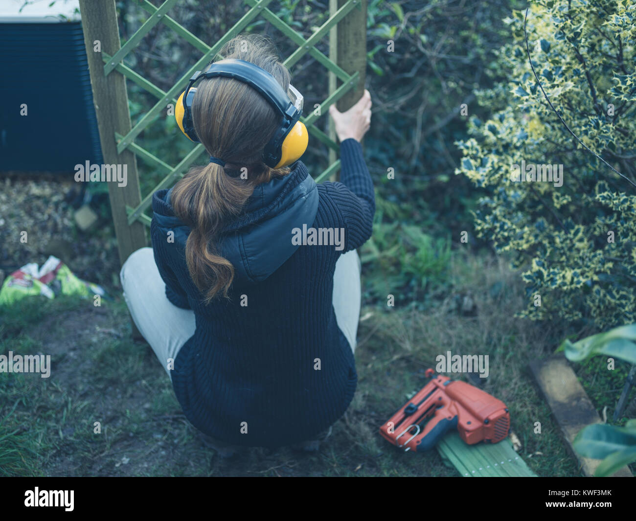 A young woman wearing ear muffs is building a fence in her garden Stock Photo