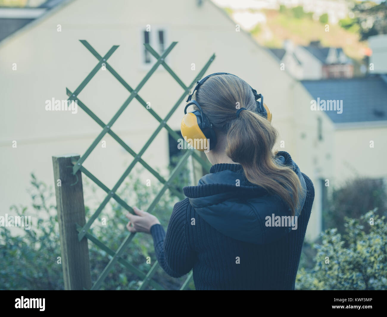 A young woman wearing ear muffs is building a fence in her garden Stock Photo