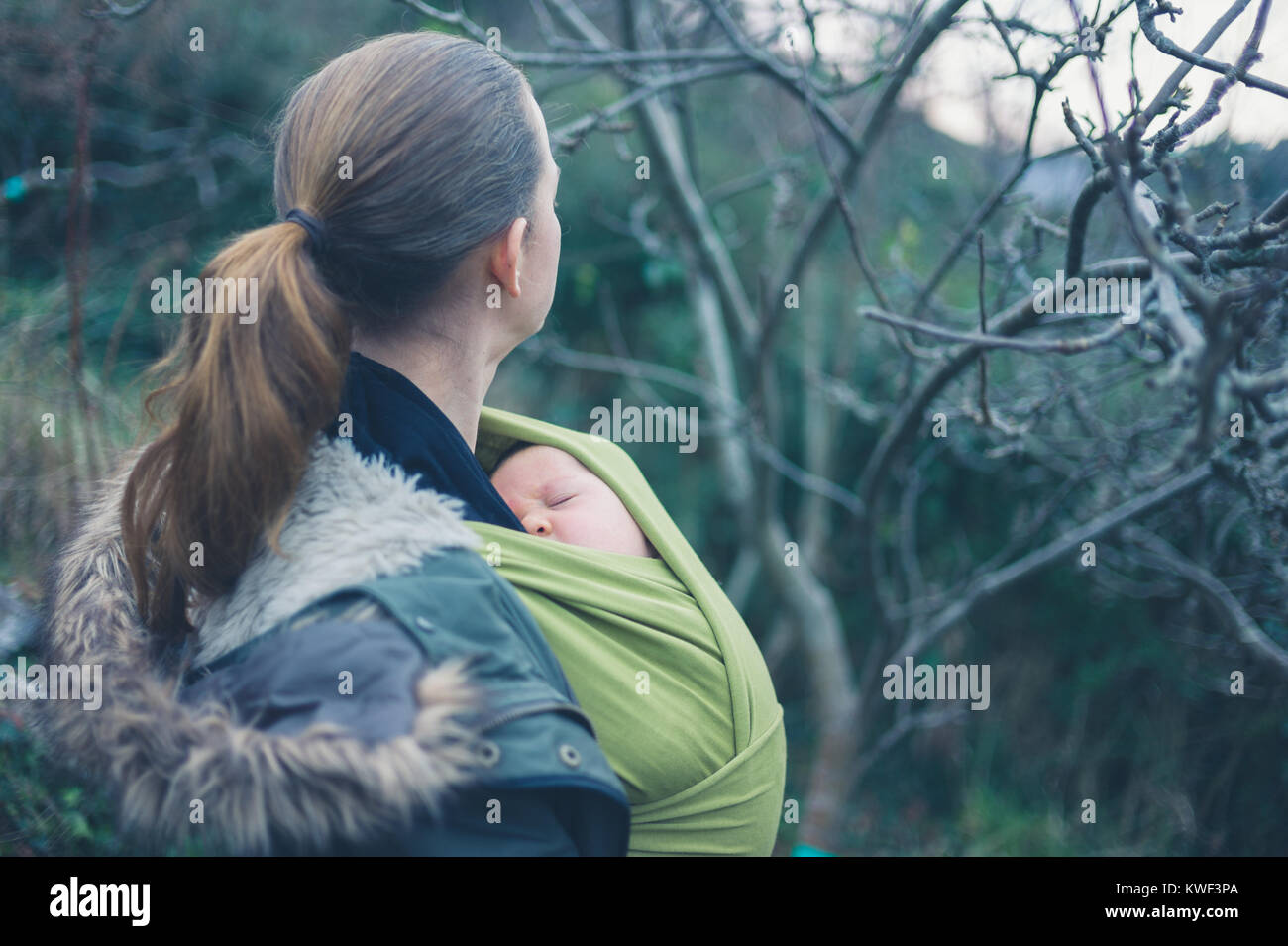 A young mother with her baby in a sling is walking in nature Stock Photo