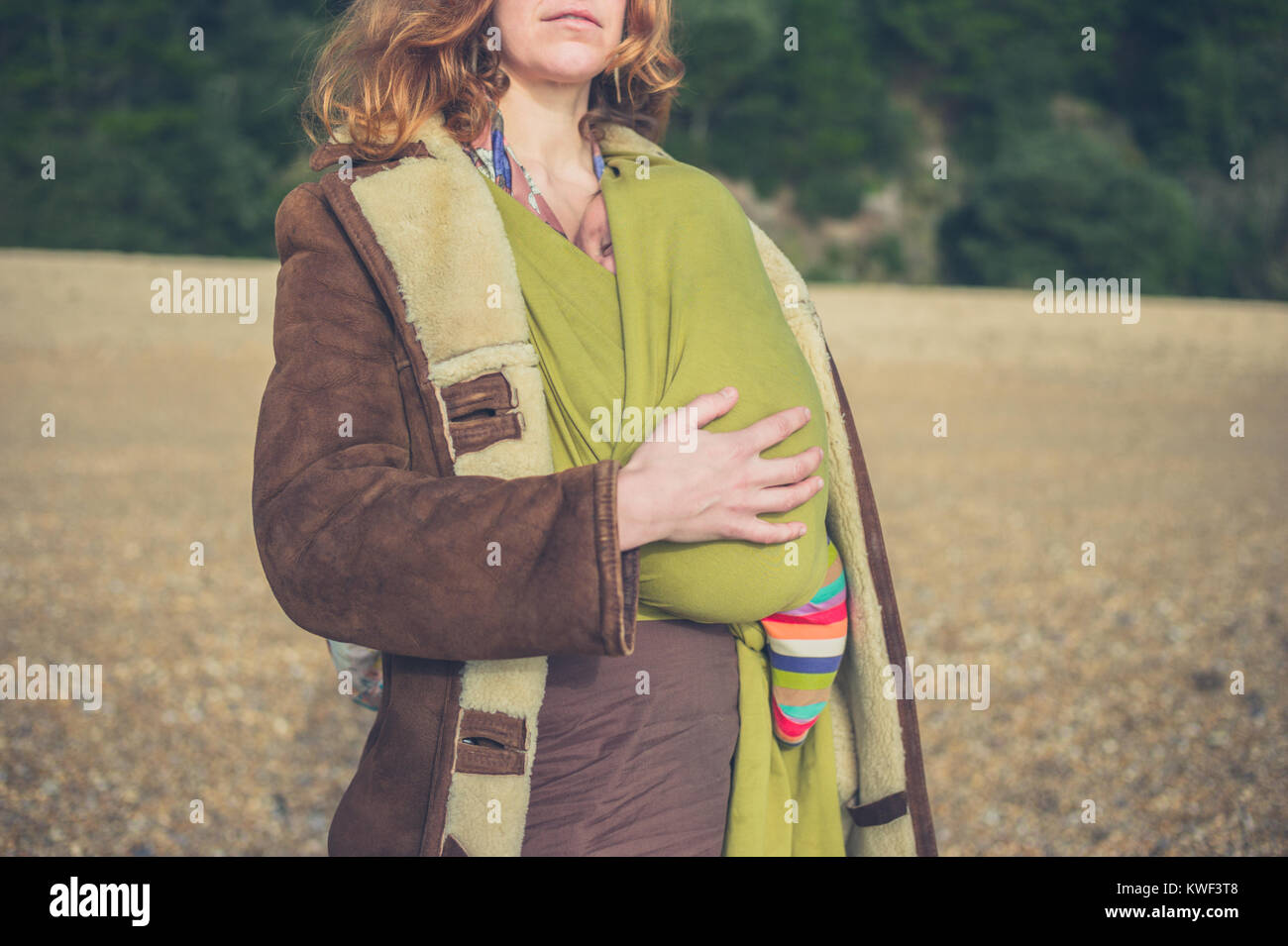 A young mother is standing on the beach with her baby in a sling on a winter day Stock Photo
