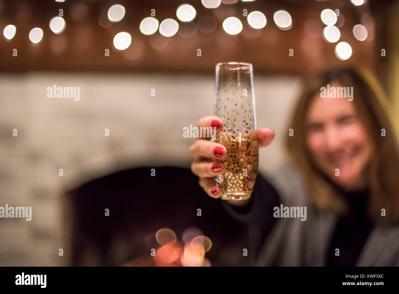 woman holding glass of champagne in front of fireplace on New Year's Eve Stock Photo