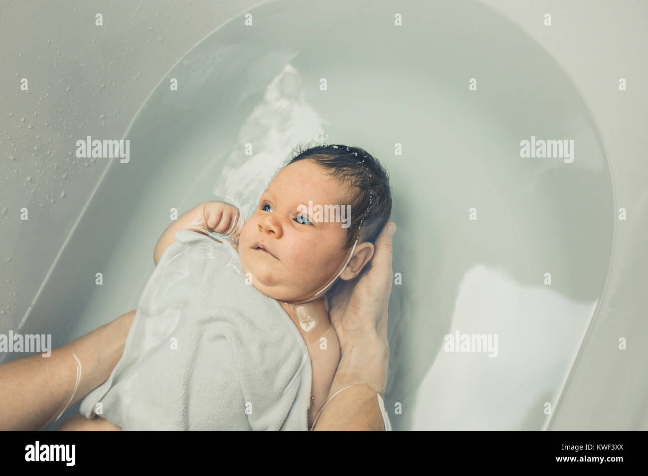 A small baby is being bathed in the bathtub by its mother Stock Photo