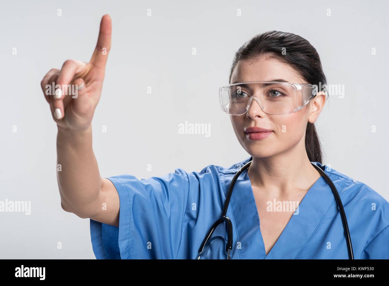 Technology inspires. Pensive satisfied female doctor  rising finger and smiling while gazing straight Stock Photo