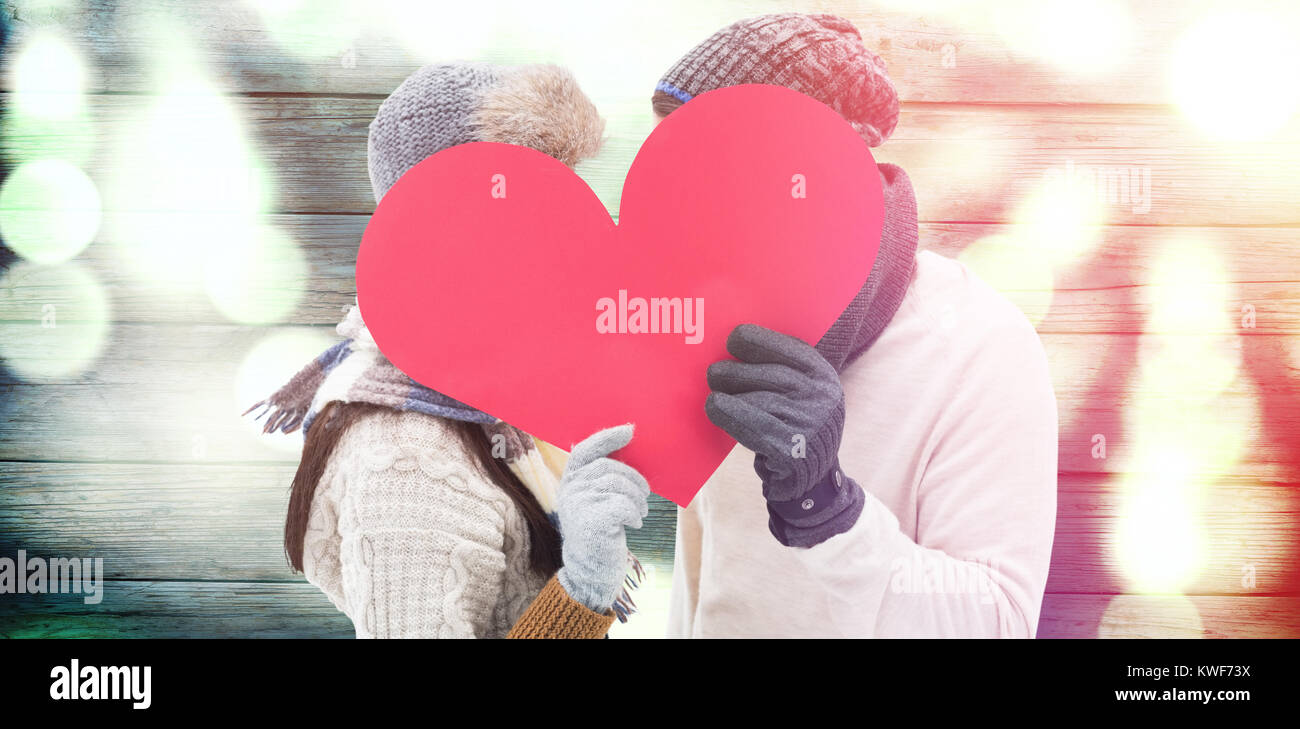 Composite image of attractive young couple in warm clothes holding red heart Stock Photo