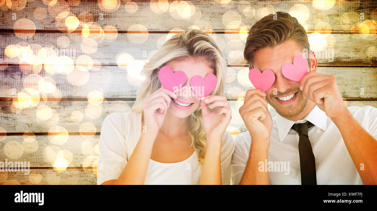 Composite image of attractive young couple holding pink hearts over eyes Stock Photo