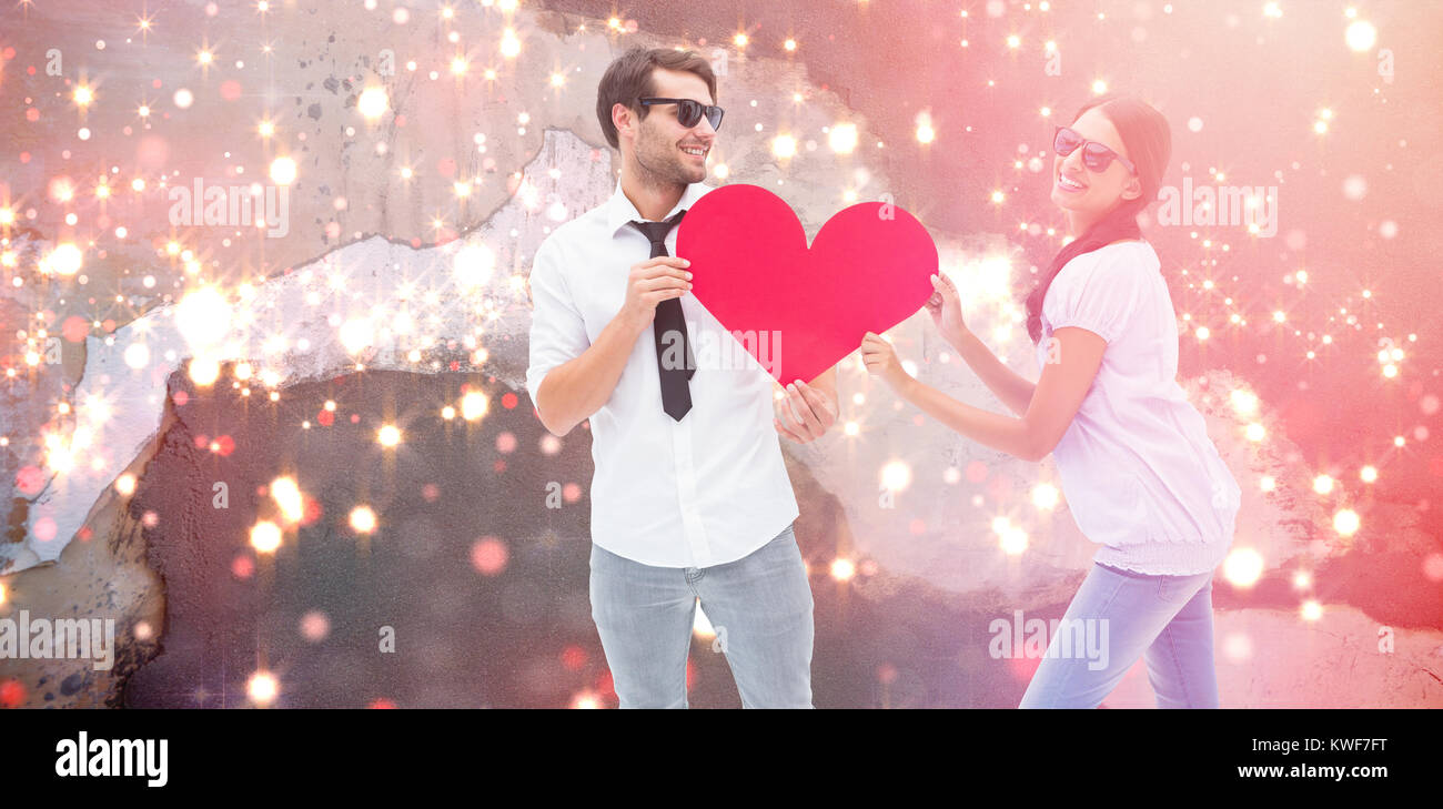 Composite image of hipster couple smiling at camera holding a heart Stock Photo
