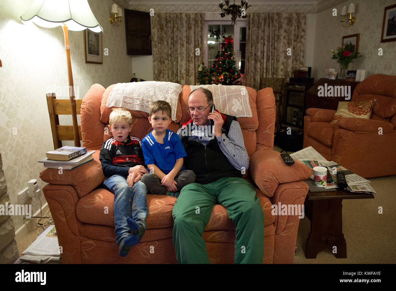 Grandfather with his grandsons making a telephone call to relatives over the festive season, siting together in the living room of their home, UK Stock Photo