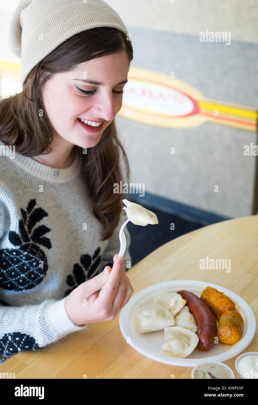 A pretty brunette girl enjoys a platter of perogies, cabbage rolls, and a smokie from Baba's Homestyle Perogies in Saskatoon, Saskatchewan, Canada. Stock Photo