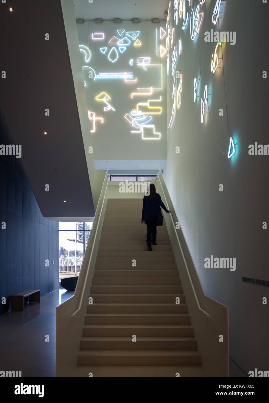 A young woman walks up stairs featuring a neon light installation named Lucky Charms by artist Pae White at the Remai Modern Art Gallery. Saskatoon. Stock Photo