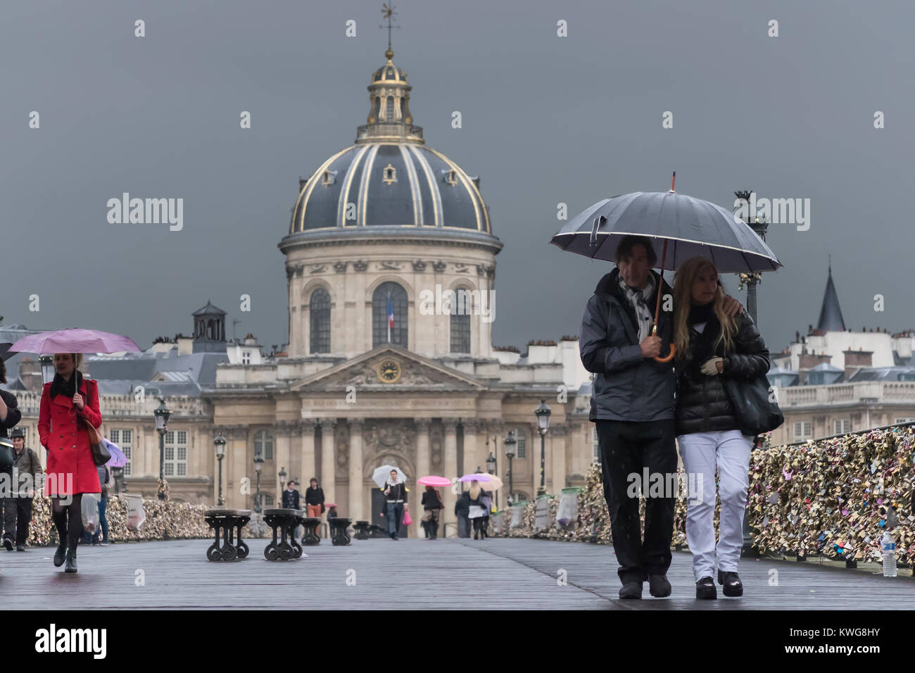 France, Paris, Couple walking in rain on the Pont des Arts, i'Intitut de France behind Stock Photo