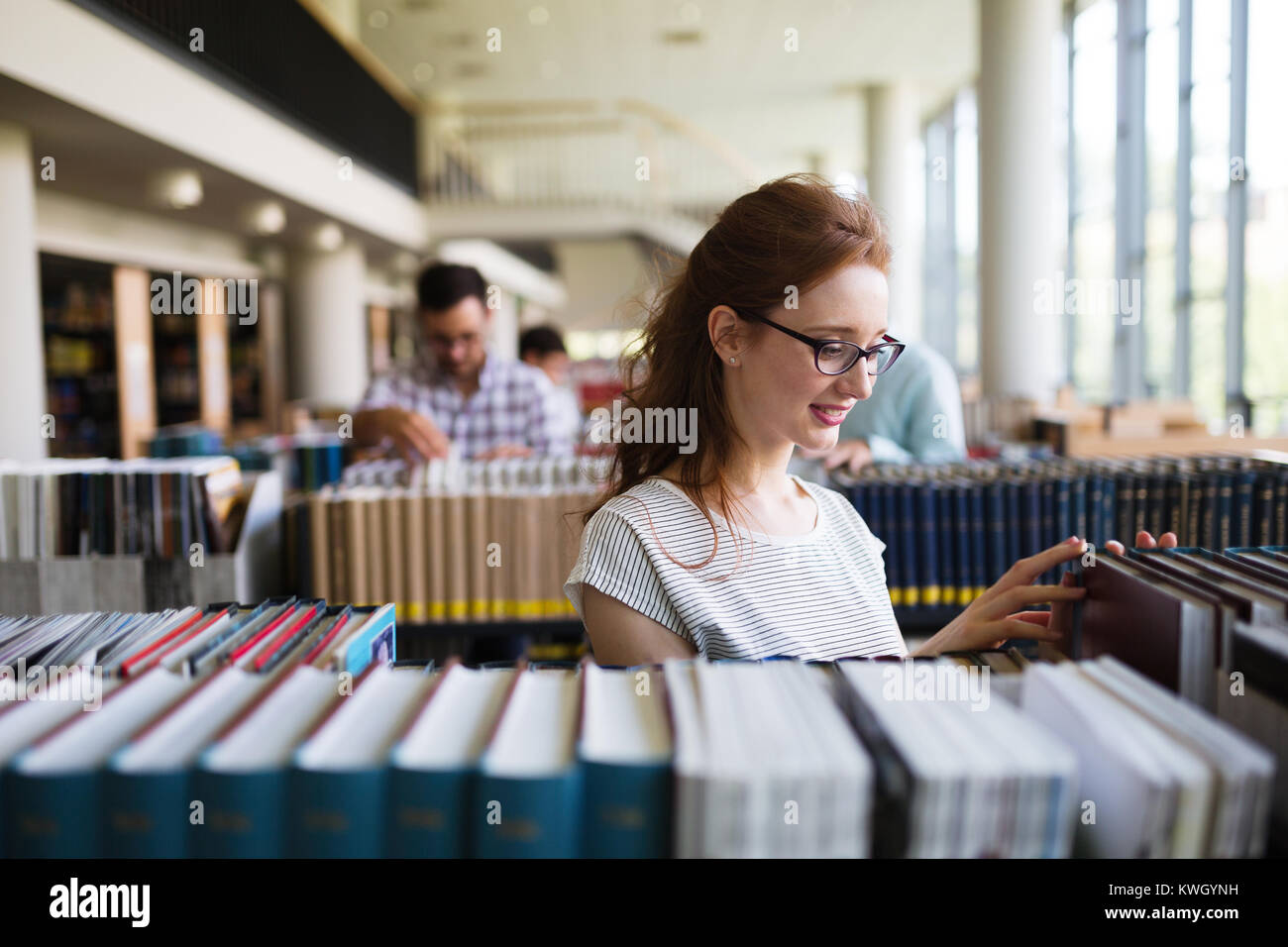 Portrait of a pretty smiling girl reading book in library Stock Photo