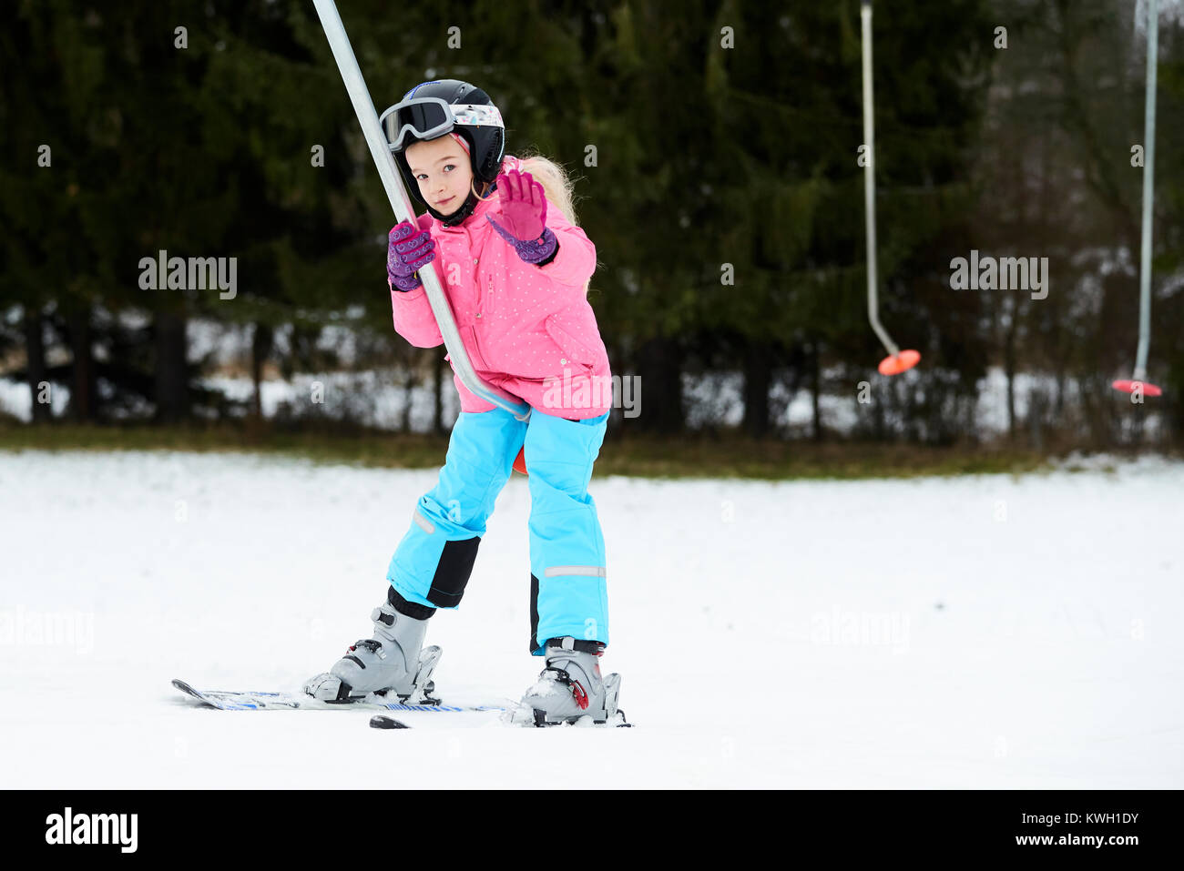 Child girl on a button ski lift going uphill in the mountains. Kids in