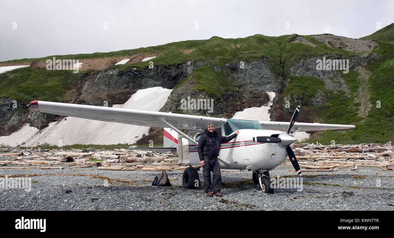 K-Bay Air airplane (Cessna 206) and pilot standing on a beach filled with driftwood in the Katmai National Park and Preserve, Alaska, US Stock Photo
