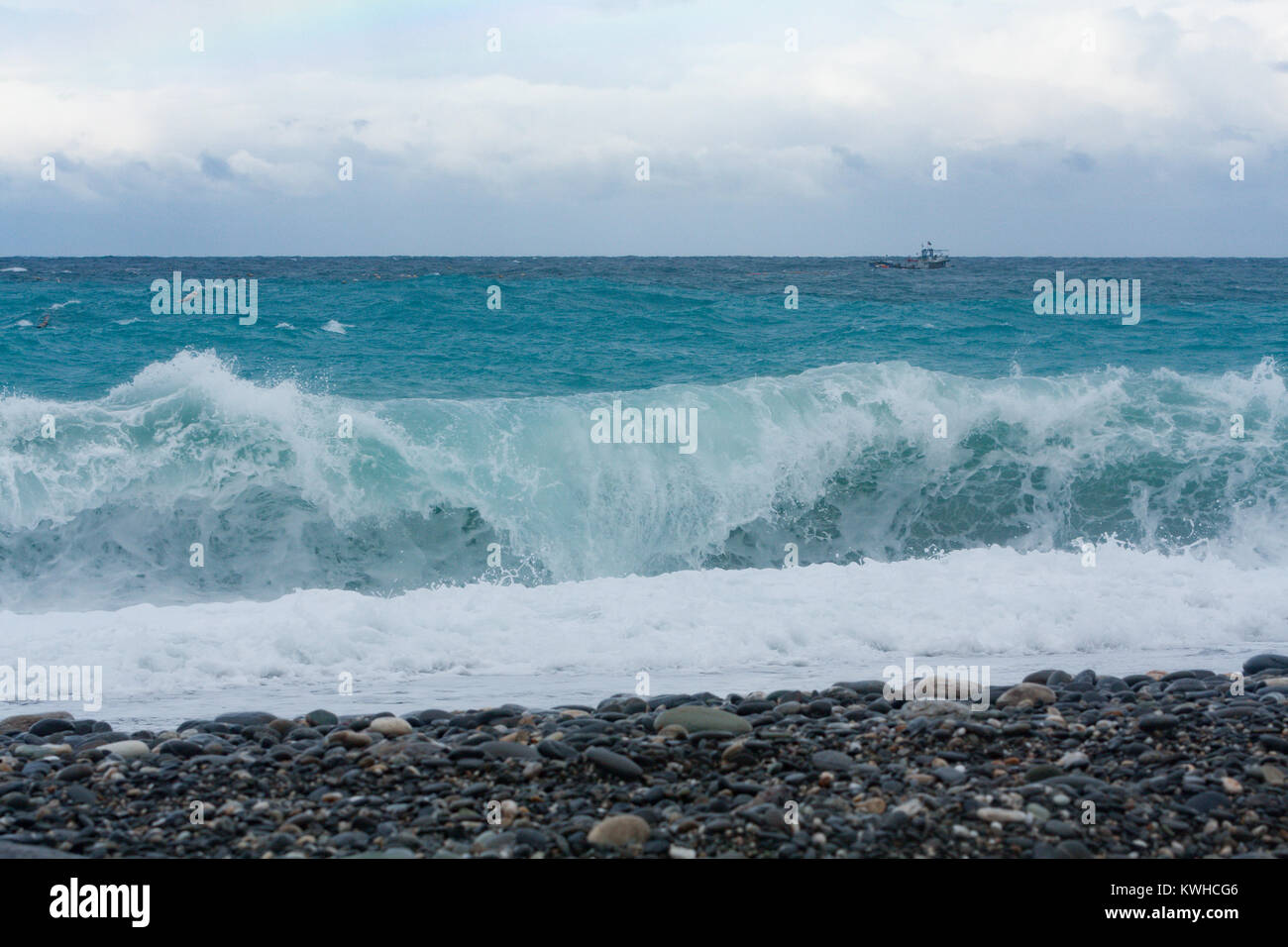 Fishing boat sailing in the sea behind plunging or dumping wave, view from pebble beach, Chisingtan Scenic Area, Xincheng Township, Hualien, Taiwan Stock Photo
