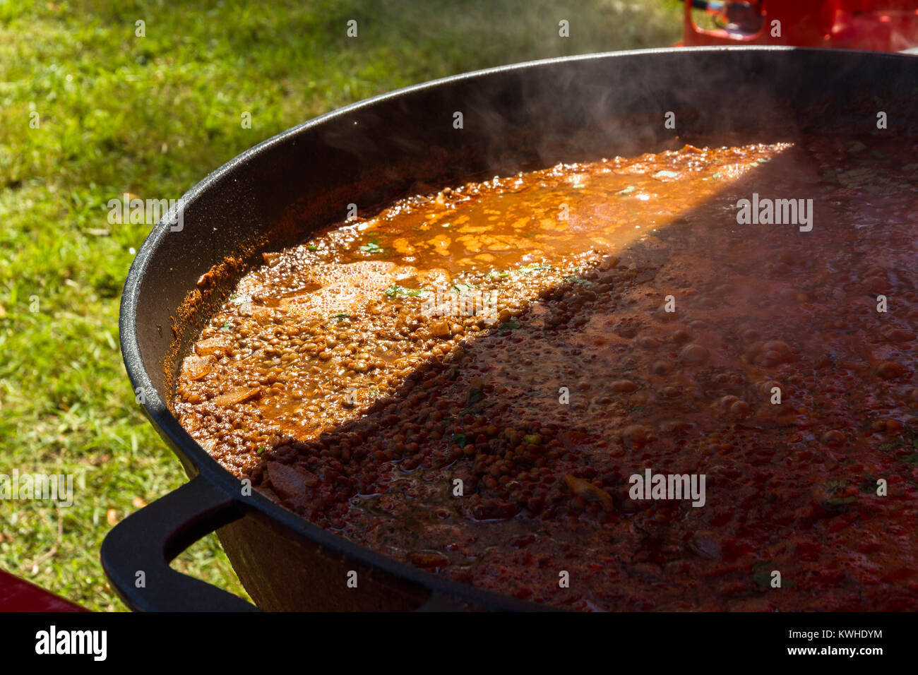 Part shade and sunshine, chilli con carne cooking in a commercial paella pan. Stock Photo