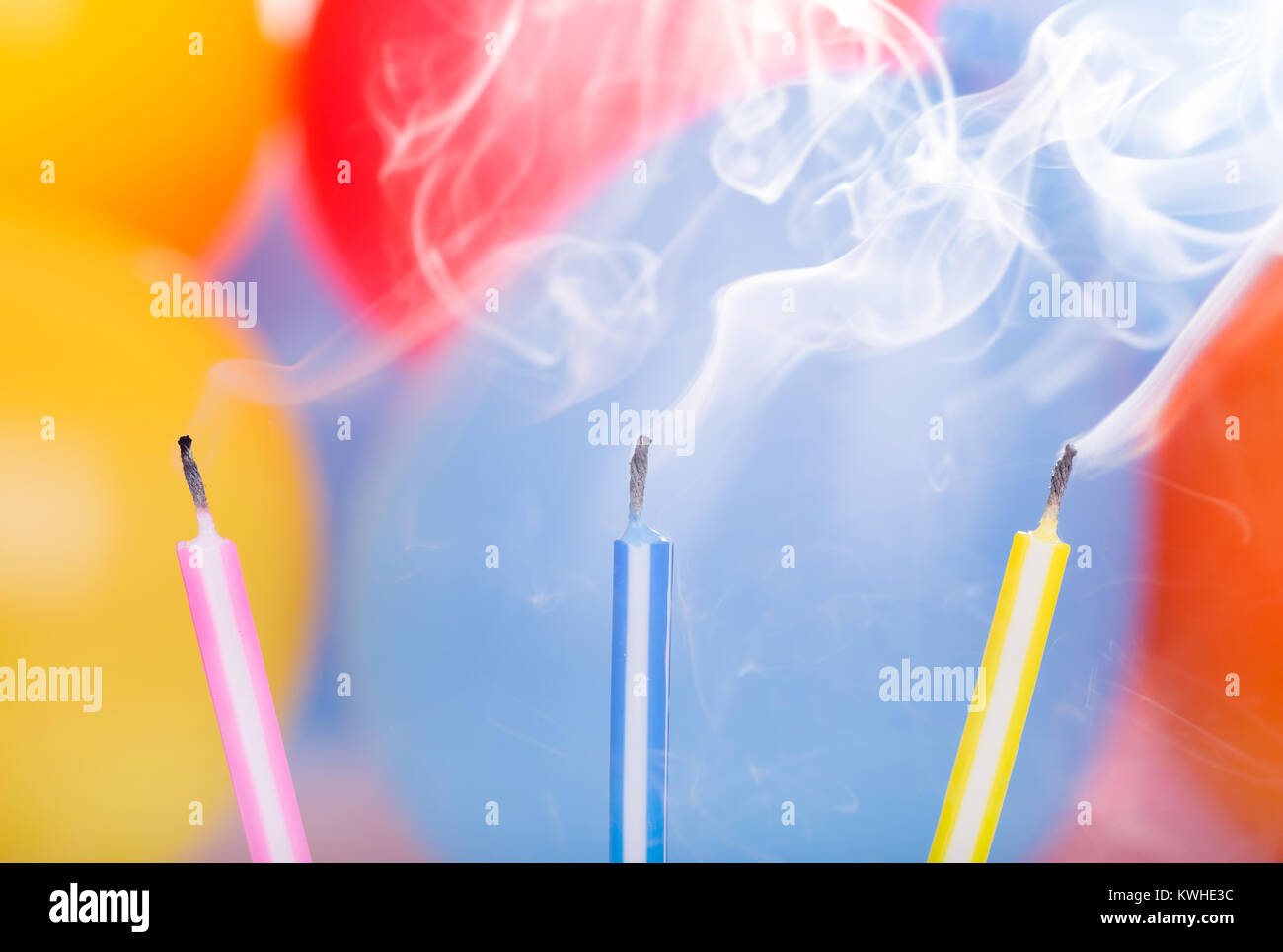 Three colorful birthday candles and smoke with balloons in background
