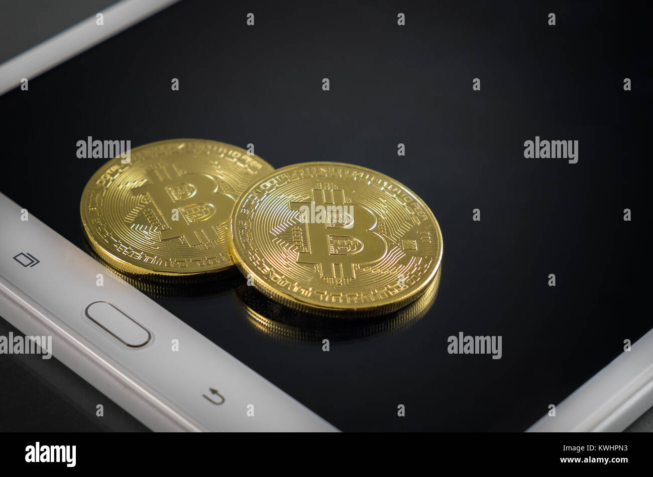 Cryptocurrency physical colored bitcoin coins. Two golden bitcoin with tablet background. Stock Photo