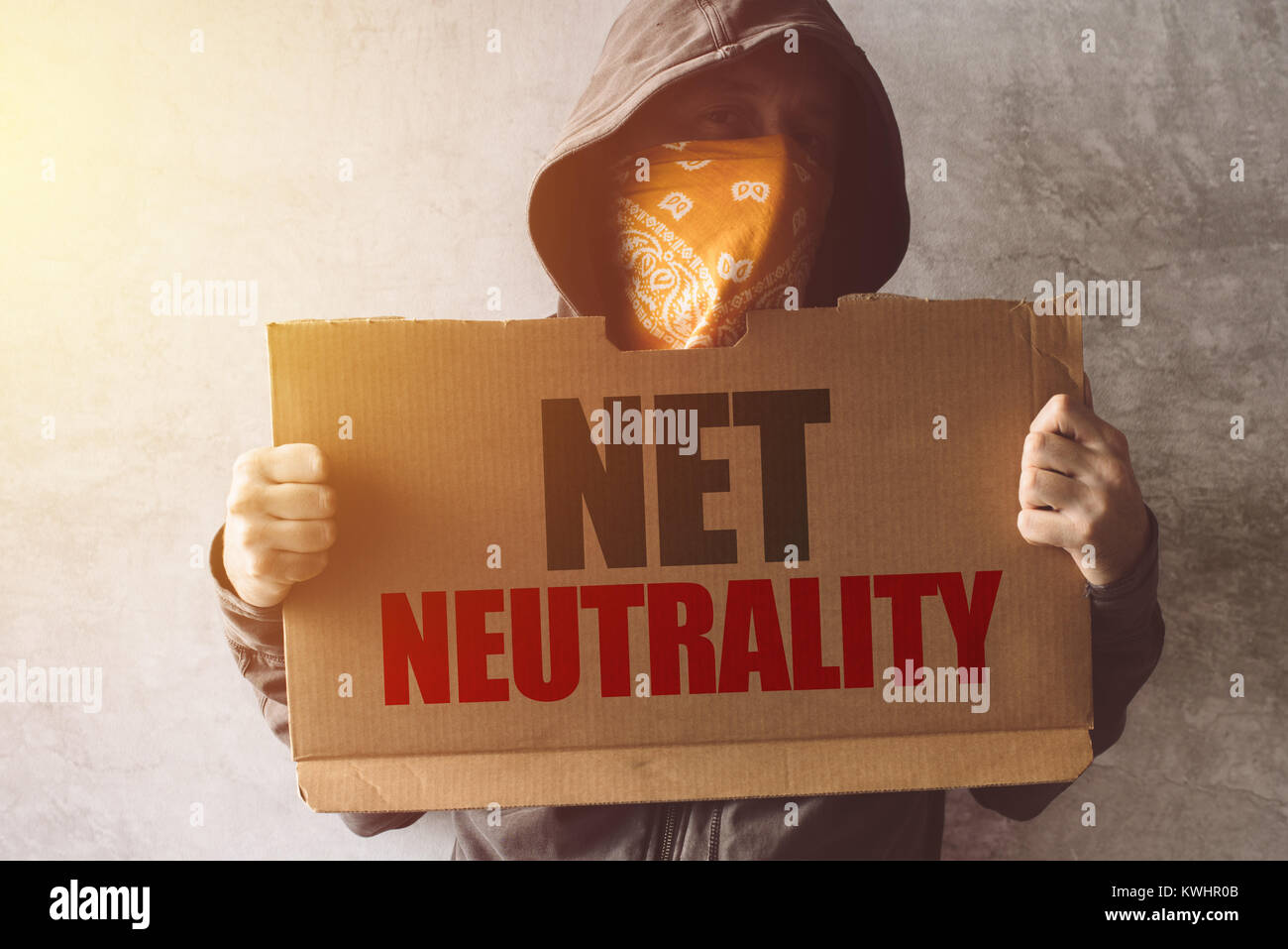 Hooded activist protester holding Net neutrality protest sign. Man with hoodie and scarf over face taking part in activism and fighting for the cause. Stock Photo