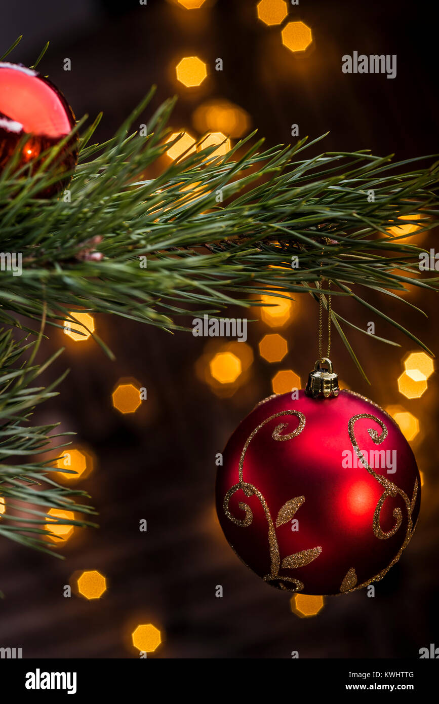 Red bauble hanging from christmas tree with festive lights out of fucus in background. Stock Photo