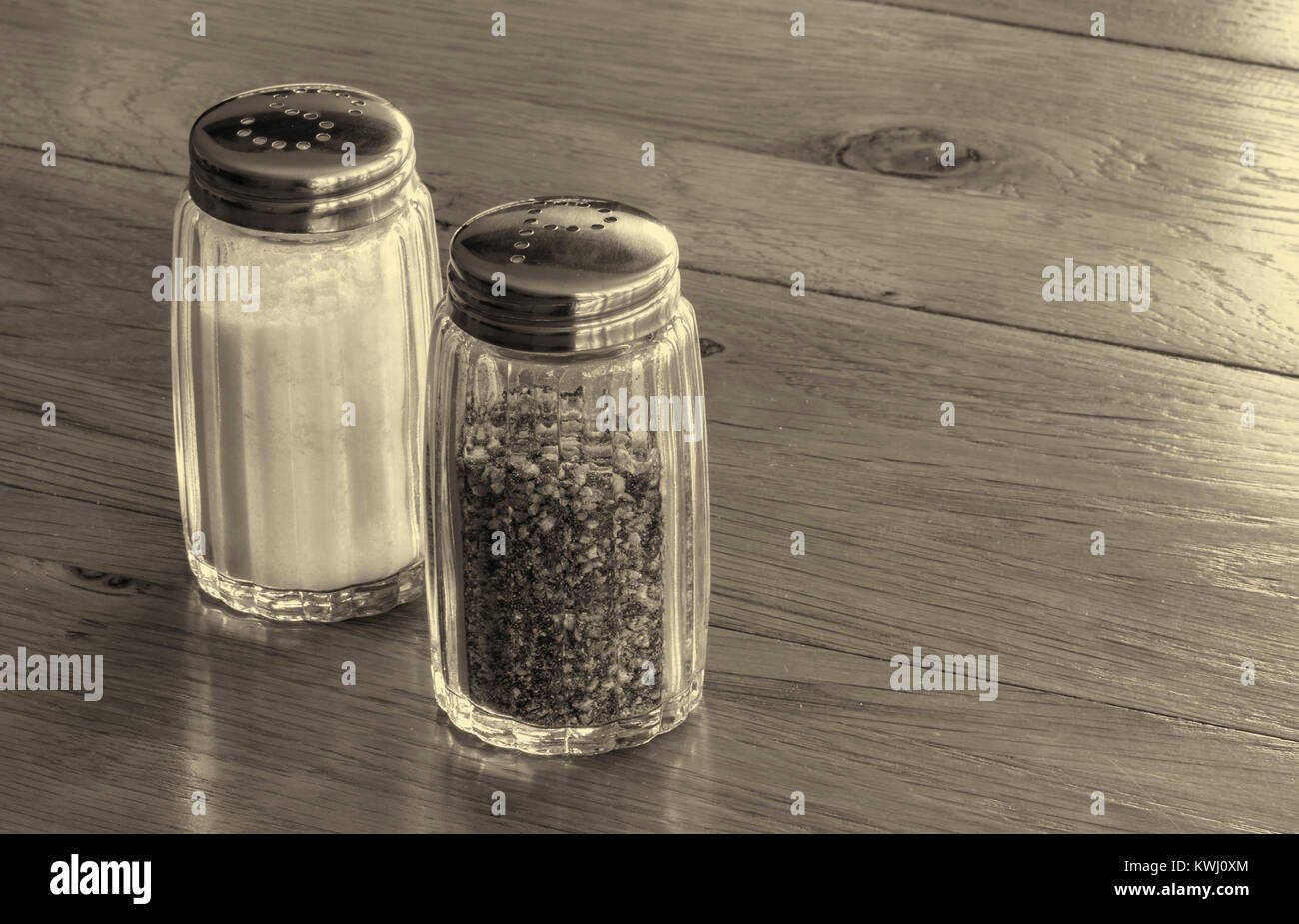 Close up of glass salt and pepper shakers or salt and pepper pots on a wooden table . Stock Photo
